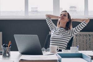 Young businesswoman holding hands behind head and smiling while sitting at her working place