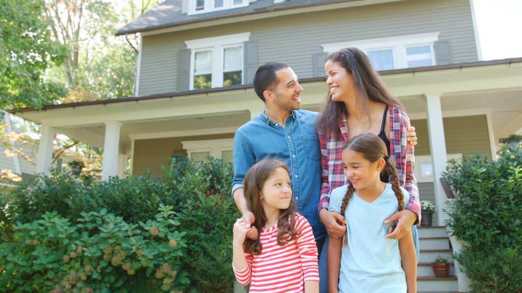 Portrait Of Smiling Family Standing In Front Of Their Home