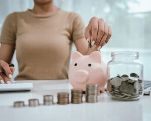 An Asian woman plans to divide her money into coins and a piggy bank, symbolizing budgeting, financial planning, saving, and smart money management.
